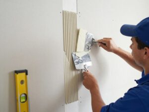 Fachowiec klejący płytę gipsowo-kartonową do ściany z widocznymi narzędziami i materiałami