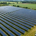 Farma fotowoltaiczna z tysiącami paneli słonecznych na terenie gruntów rolnych, inwertery sieciowe widoczne z przodu instalacji